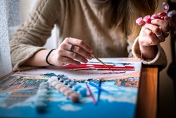 Painting for beginners, a woman draws a picture by numbers with acrylic paints on canvas,painting a picture with a brush, a girl draws a picture, self-isolation, home hobby, creativity at home