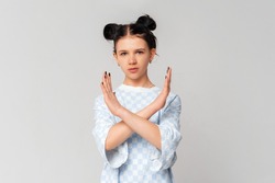Serious dark-haired teen girl crossing arms and palms doing negative sign, prohibit, forbid smth bad, standing in trendy t shirt over light grey background. Social distancing