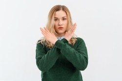 Please, do not, stop. Young serious woman with fair-haired in casual clothes, crossing arms and palms doing negative sign, prohibit, forbid something bad. Indoor studio shot on white background