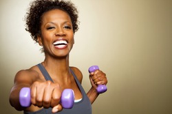 Happy African American fitness woman lifting dumbbells smiling and energetic. 
