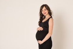 Portrait shot of a young beautiful woman in the second trimester of pregnancy on a monochrome background. Close-up of a pregnant woman in casual clothes with her hands on a round stomach. 