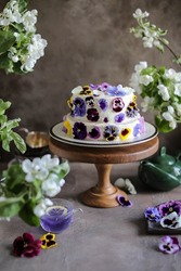 Very beautiful two-tier cake with curd cream decorated with edible viola flowers. Cake with spring flowers on a high wooden stand.