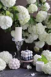 Beautiful candles made of natural soy wax on wooden stands among white blooming viburnum. Interior candles and flowers for the home.