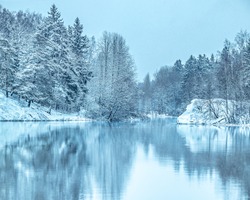 Winter landscape of snow covered trees reflected in the mirrored surface of frozen lake. January scenery. Cold frosty day. Beautiful scene of the snowy coastline with forest. Ice on a frozen river.