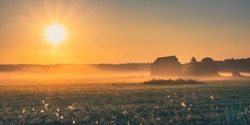 Misty morning at countryside. Sunrise over field. Rural landscape. Yellow sunshine and sunlight in hazy meadow. Sun rising over a foggy field with lonely barn. Vibrant sunrays of light Fog Mist Nature