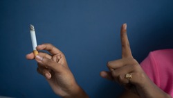 Portrait of a girls one hand holding a cigarette and gesturing to stop with her finger | Quit smoking cigarettes concept