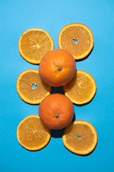 Orange slices parallel to each other with two whole oranges centered in a vertical photo on a blue background.