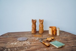 Two homemade toy cats stand on the work surface. Toys are made of wood, around lie tools for carving wood and lying sawdust. Creative pursuits, wood carving. High quality photo