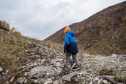 A little boy in a blue jacket climbs uphill. A young tourist conquers the top of the mountain. Walk the trail. Children's tourism. High quality photo