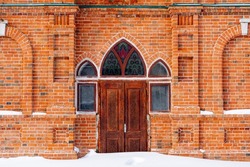 Entrance to a brick building. Arched windows and doors. Heavy wooden door and stained glass windows. Snowdrifts in front of the entrance. High quality photo