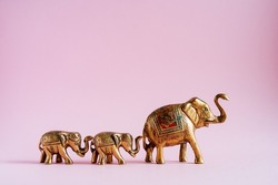 Golden elephant figurines on a pink background. A family of Indian elephants. Sacred animals in India. Luck and stability in the house by elephant's energy. High quality photo