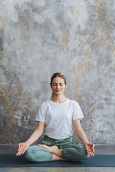 Happy girl in a tracksuit, sits on the floor in the lotus pose. A lady meditates,crossed fingers in Yoga Mudra. Assanas for Meditation and Relax. High quality photo