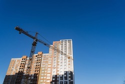 A crane builds a house at a height, lifts the load to the upper floor. The construction site of a residential building, a building against the sky. High quality photo