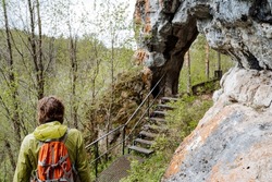 Hiking with a backpack in the mountains, tourist eco-route in the park, Hole passage in the rock, metal stairs through the stone, trekking in nature. High quality photo