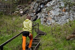 The view behind a person climbs the stairs up against the background of the rock, hiking in the forest walking, wooden old stairs, rotten steps, taking a foot step. High quality photo