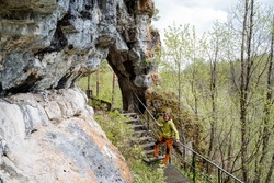 A hole in the rock through the passage through the mountain, an eco trail a hiking route, a metal staircase in nature, a guy stands in the mountains, a tourist leaning on the railing