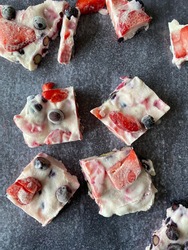Frozen yoghurt berry bars with blueberries and strawberries made with yoghurt, honey and lime juice on a black slate backdrop