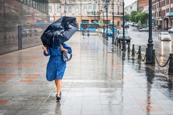 Woman in bad rainy weather walks down the street and tries to keep the umbrella from the strong wind. City landscape in rainy weather. City scenes in the rain.