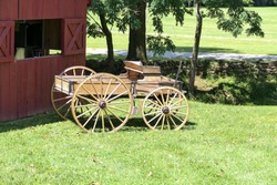 An antique wooden horse cart is parked in front of a barn
