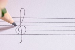 
Female hand writing bass clef on white paper holding black pencil