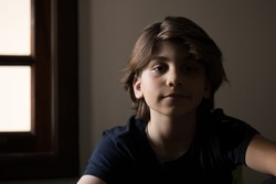 Portrait with shadows on the face of a 10 year old boy with long hair.