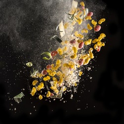Explosion of ingredients for Italian kitchen (tomato, pasta, cheese, chopping board and knife) isolated in the air on black background