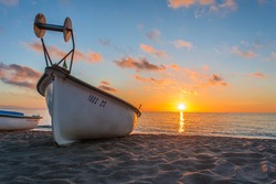 Small fishing boat on beach at sunset.