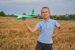 a boy launches an airplane in a field,a boy in glasses holds and plays with an airplane in a wheat field