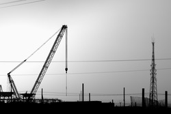 Silhouette of lattice boom crawler crane at construction site in oilfield at sunset - black and white 