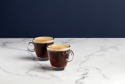 Two glass coffee cup with espresso in morning on white marble background. Aroma, ristretto. Mug of coffee. Close up. Blue wall