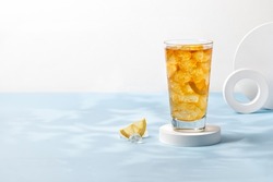 Delicious refreshing summer drink, iced tea in a glass on podium. Sunshine, blue background. Copy space. Ice tea, lemonade