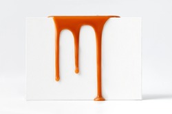 Dripping caramel drops of sweet caramel sauce on white podium on white background.  Melted caramel sauce drip, drops of sweet liquid toffee.