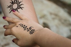 A woman's hand with a henna Mehndi flower tattoo touches a man's hand with a henna Mehndi sun tattoo