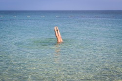 A woman plunging in turquoise sea water. Feet sticking out of the water