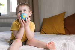 Child boy with blonde hair hugging the earth globe, save the earth concept. 3 years old kid holding a toy globe model. Baby toddler. Early, age children education development.