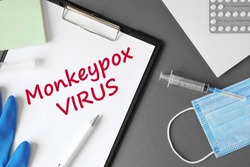 The word Monkeypox VIRUS on Gray modern doctor desk table background. Mask, notepad, syringe, blue gloves and supplies. Monkey pox spreading. Medicine and healthcare, medical education. Top view.