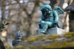 photograph of a bronze sculpture (statue) of a child angel in Père Lachaise cemetery (in Paris). The angel is holding his head with one hand.