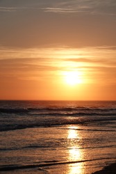 Sunset over the Atlantic Ocean. The sun comes out of the clouds. The sky varies from yellow to orange and is reflected on the waves of the sea.
