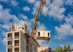 Crane lifting a wooden building module to its position in the structure. Construction site of an office building in Berlin. The new structure will be built in modular timber construction. 