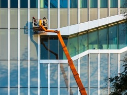 Cleaner worker using a cherry picker to clean a glas facade of a contemporary office building.