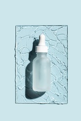 Glass bottle with pipette of cosmetic liquid transparent gel on blue background. Top view, flat lay.