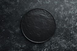 Black plate on black stone background. Top view. Free space for your text.