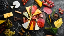 Appetizers table with italian antipasti snacks and wine in glasses. Cheese, wine, salami and prosciutto on a black stone background. Top view. Free space for your text.
