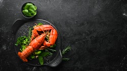 Boiled lobster with vegetables on a black stone plate. Seafood. Top view. Free space for your text.