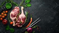 Poultry meat. Fresh raw duck thigh with rosemary and spices. On a black stone background. Top view.