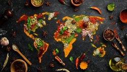 Set of spices and herbs. Indian cuisine. World map: Pepper, salt, paprika, basil, turmeric. On a black wooden board. Top view. Free space for copying.