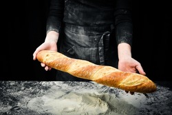 Fragrant fresh baguette in hands. Black cooking background. Isolated on black background.