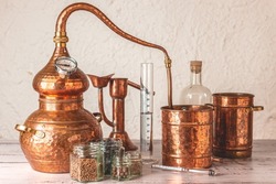 Copper alembic used for distilling with botanicals, juniper, cardamom and accessories on a wooden table.
