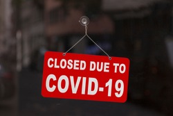 Close-up on a red closed sign in the window of a shop displaying the message 