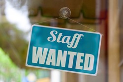 Close-up on a blue open sign in the window of a shop displaying the message: Staff wanted.